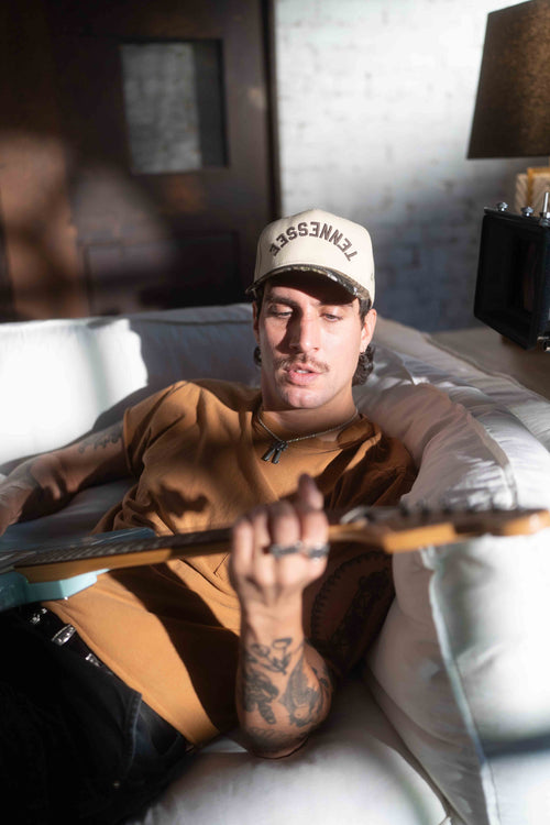 Person with guitar in custom made hat with Tennessee on a white couch